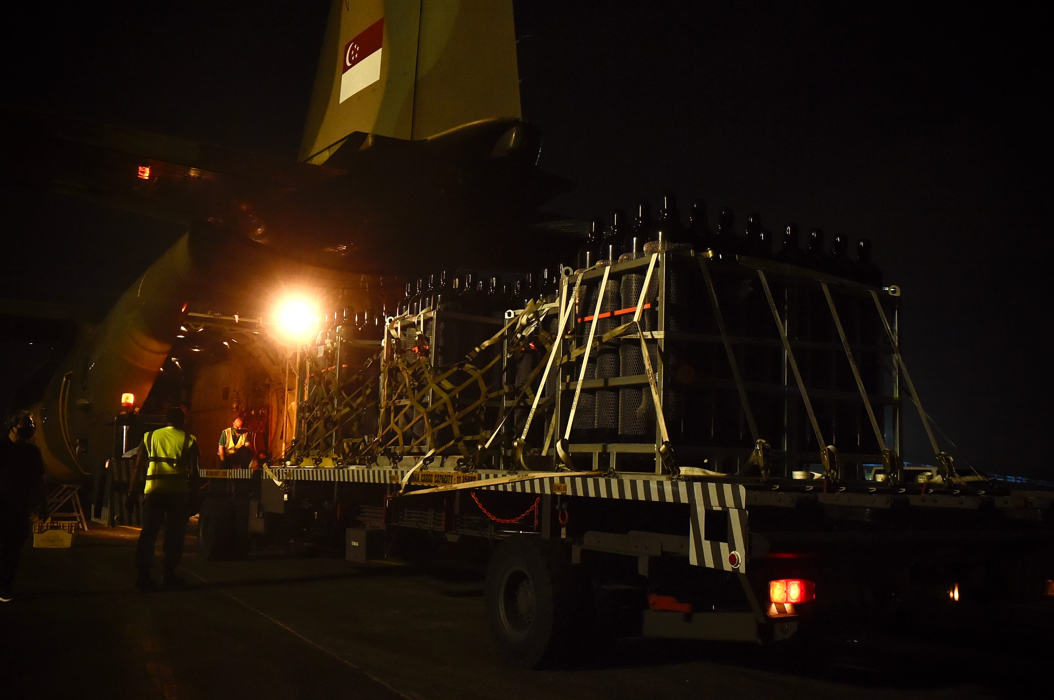 Singapore Air Force plane being loaded with containers by workers at night.